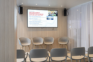 The presentation area fully prepared with a stage, empty seating, and the formal agenda for the upcoming expert talks displayed on a large screen.