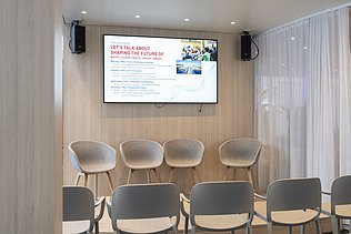 Der Präsentationsbereich ist mit einer Bühne, leeren Sitzplätzen und der auf einem großen Bildschirm angezeigten offiziellen Tagesordnung für die anstehenden Expertengespräche vollständig vorbereitet.
