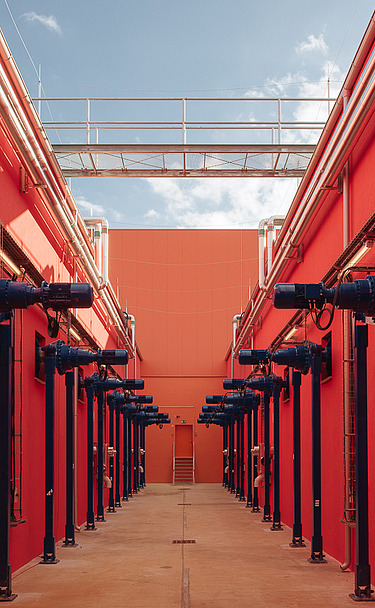Symmetrical corridor with vibrant red walls and blue mechanical units. This specialized industrial space features a high ceiling with a walkway and is designed for automated technical processes.