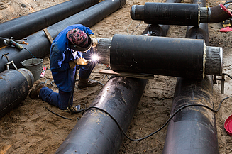 A welder working on underground steel pipelines at a construction site.