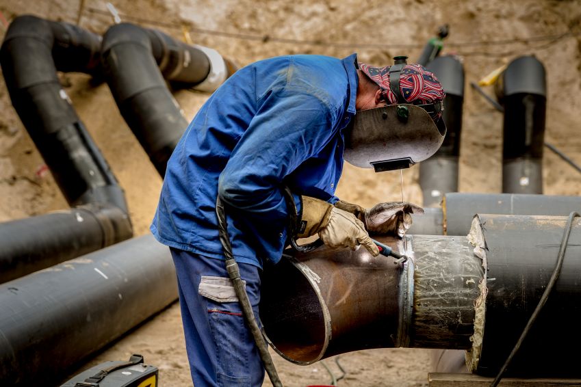 A worker welding large metal pipes at an industrial construction site, wearing protective gear and focusing on precision wor