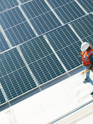 An aerial, high-angle shot shows two technicians wearing white hard hats and orange safety vests walking across a bright rooftop.