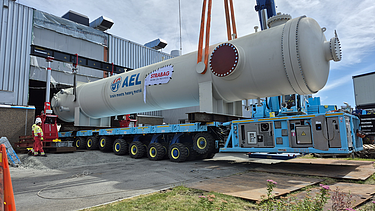 Crane-assisted lift of a large AEL condenser vessel from a multi-axle heavy transport vehicle outside the installation building.