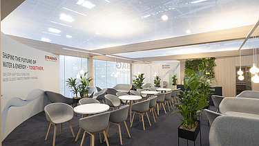 A dynamic perspective of the upper floor's glass facade featuring the STRABAG logo and hanging greenery.