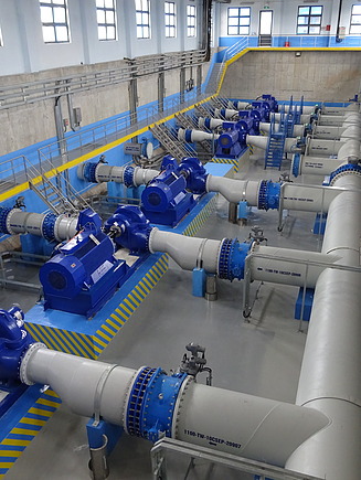 Innenansicht einer Wasseraufbereitungsanlage mit großen blauen Pumpen und grauen Rohrleitungen, die in parallelen Reihen angeordnet sind.