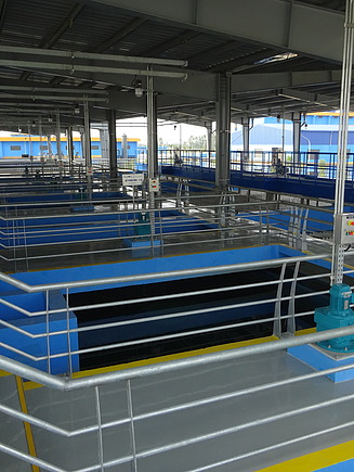 Überdachter Teil einer Kläranlage mit mehreren rechteckigen Becken, Metallgeländern und blauen Strukturelementen.