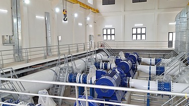 Innenansicht einer Pumpstation in der Oberflächenwasseraufbereitungsanlage Xuan-Mai mit großen blauen Pumpen, miteinander verbundenen Rohrleitungen, Zugangsplattformen und einem Laufkran.