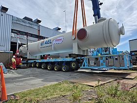 Crane-assisted lift of a large AEL condenser vessel from a multi-axle heavy transport vehicle outside the installation building.