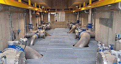 Interior view of the raw water pumping station at the Xuan-Mai Surface Water Treatment Plant, showing large water pipelines, valves, pumps, and maintenance walkways.