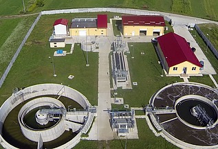 Luftaufnahme der Kläranlage von Moinești in Rumänien. Zu sehen sind runde Klärbecken, Behandlungsbecken, Kontrollgebäude mit roten Dächern und umliegende Grünflächen innerhalb eines eingezäunten Geländes.