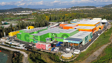 Aerial view of a large water treatment plant under construction, featuring multiple concrete structures, tanks, and surrounding green landscape.