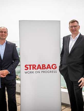 Die Vorstände von STRABAG und WTE Wassertechnik posieren für ein Gruppenfoto in der Donau-City-Straße. Sie stehen neben einem STRABAG-Markenschild, das die Integration der WTE in den UB4K-Teilbereich LC Wasser symbolisiert.