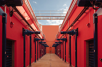 Symmetrical corridor with vibrant red walls and blue mechanical units. This specialized industrial space features a high ceiling with a walkway and is designed for automated technical processes.