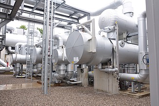 Large, insulated shell-and-tube heat exchangers and heavy-duty piping at an industrial plant. The silver-clad units are part of a thermal processing system used for energy recovery or cooling.