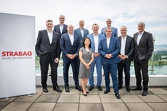 Menschen stehen für ein Gruppenfoto auf einer Terrasse mit einem STRABAG-Display und einer Stadtlandschaft im Hintergrund zusammen.