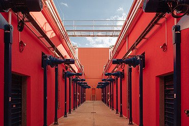 Symmetrical corridor with vibrant red walls and blue mechanical units. This specialized industrial space features a high ceiling with a walkway and is designed for automated technical processes.