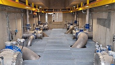 Interior view of the raw water pumping station at the Xuan-Mai Surface Water Treatment Plant, showing large water pipelines, valves, pumps, and maintenance walkways.