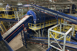 Aerial view of a large mechanical-biological waste treatment plant with green and orange buildings surrounded by landscape.