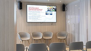 The presentation area fully prepared with a stage, empty seating, and the formal agenda for the upcoming expert talks displayed on a large screen.
