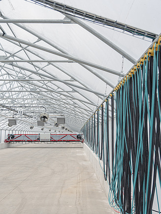 Innenansicht einer Solartrocknungshalle mit großflächigem Trocknungsbereich und automatischem Schlammwende- und Fördersystem. Die leichte Hallenkonstruktion verfügt über Belüftungseinrichtungen und seitliche Lüftungsöffnungen zur solar unterstützten Schlammtrocknung.