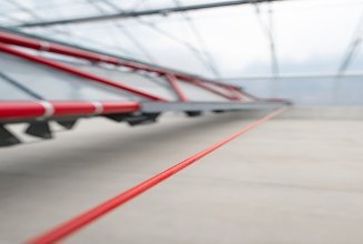 Close-up view of the automated sludge turning and conveying system inside a solar sludge drying hall. The red mechanical unit is used to loosen, turn, and transport sludge during the drying process, improving drying efficiency through regular material movement.